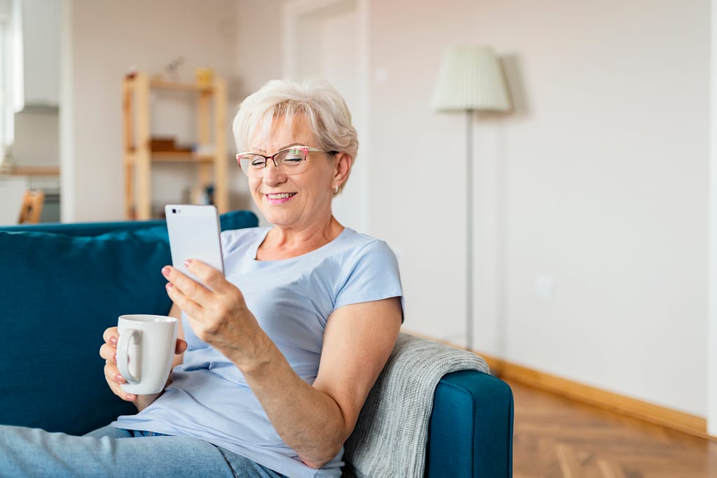 smiling senior holding coffee mug and looking at smartphone.jpg