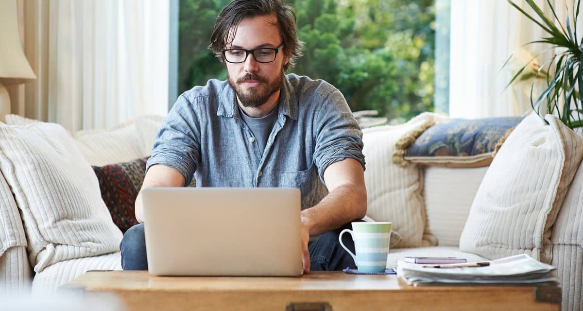 Man sitting on sofa and using laptop at home.width HXjQHwf