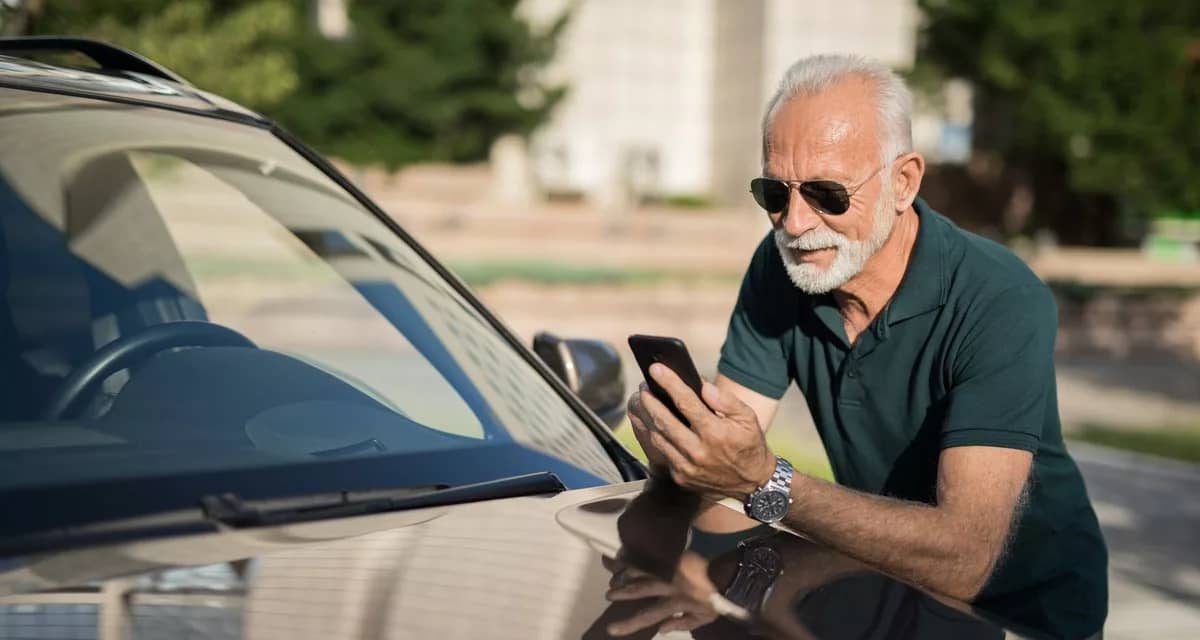 Mature man leans on car looking at phone LCHl.width .jpg