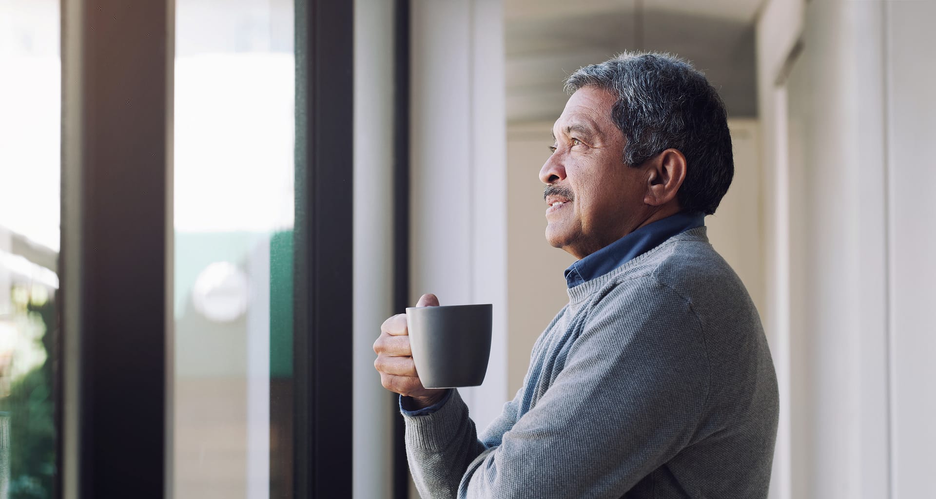 older person holding a mug and looking out a window ifSeK7