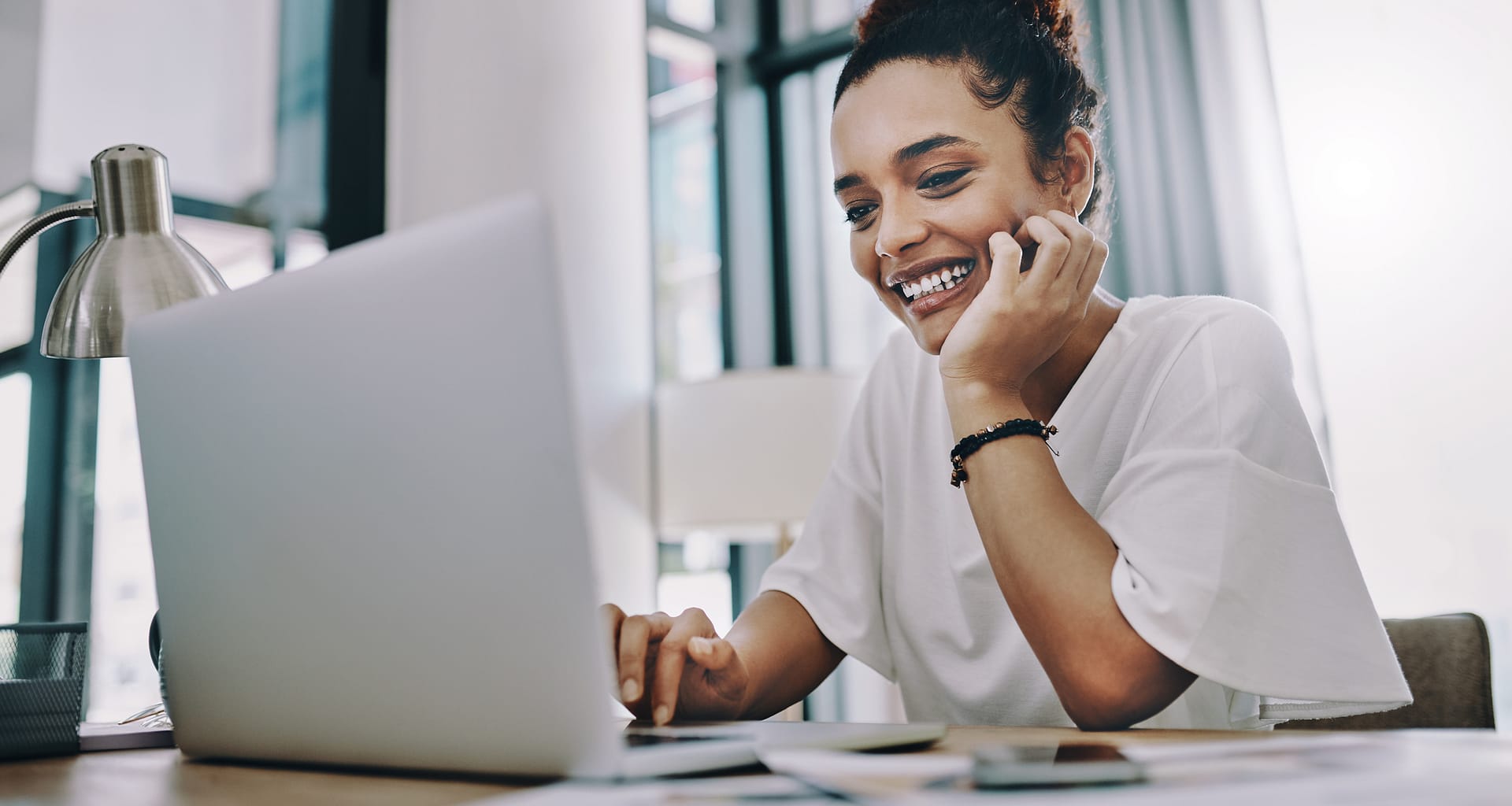 smiling young person with hand on chin looking at laptop GNDUtQ