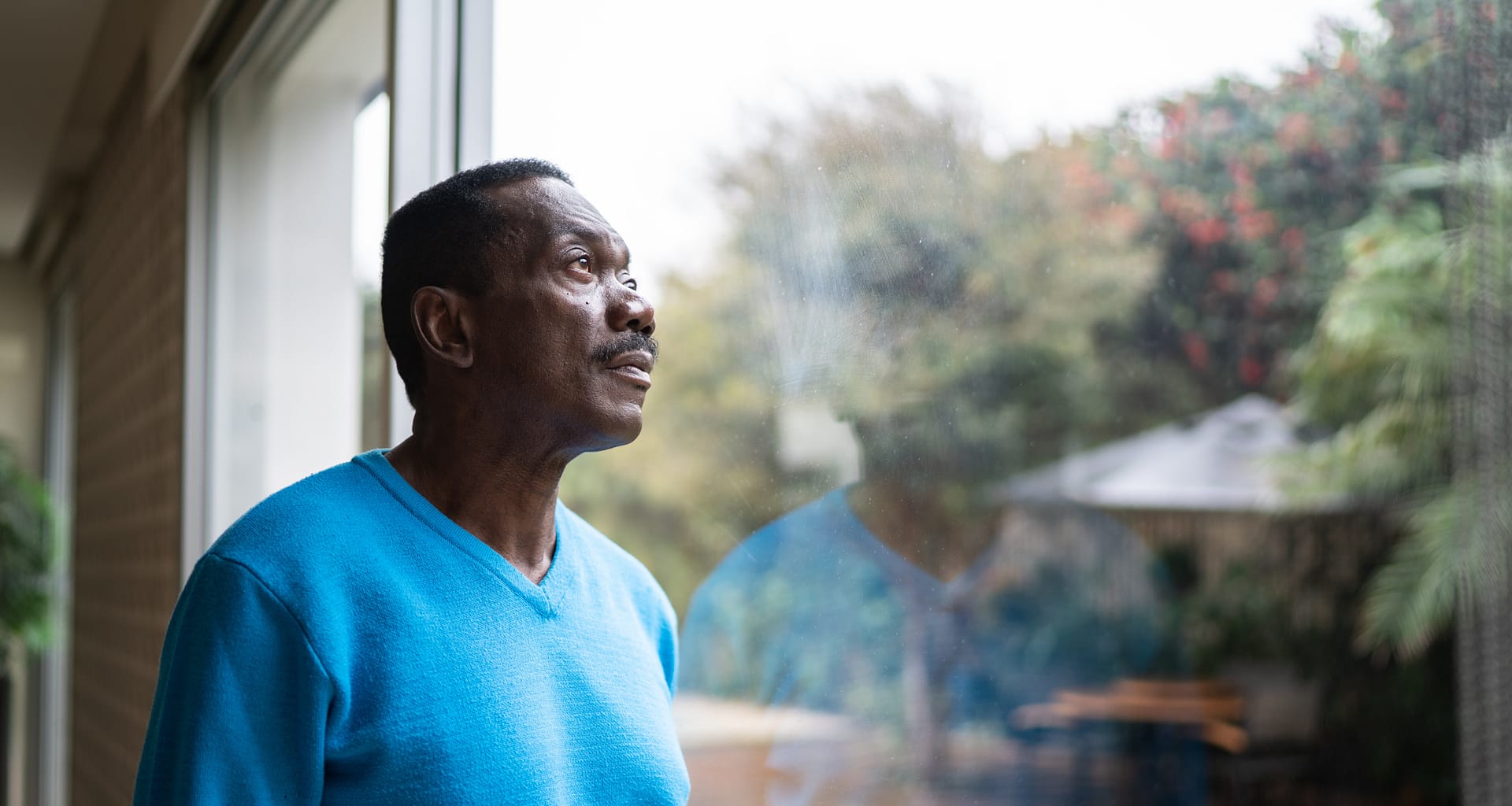 person with serious expression looking out a window