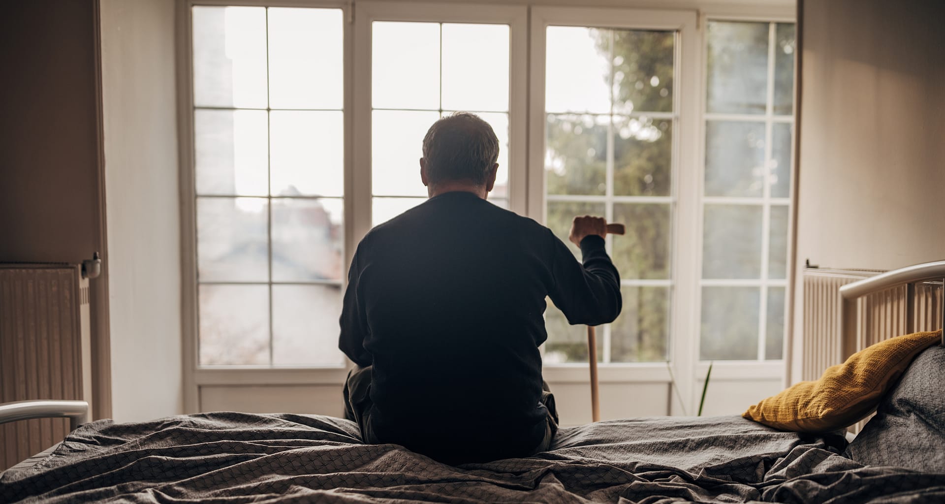 retired man with cane sitting on bed