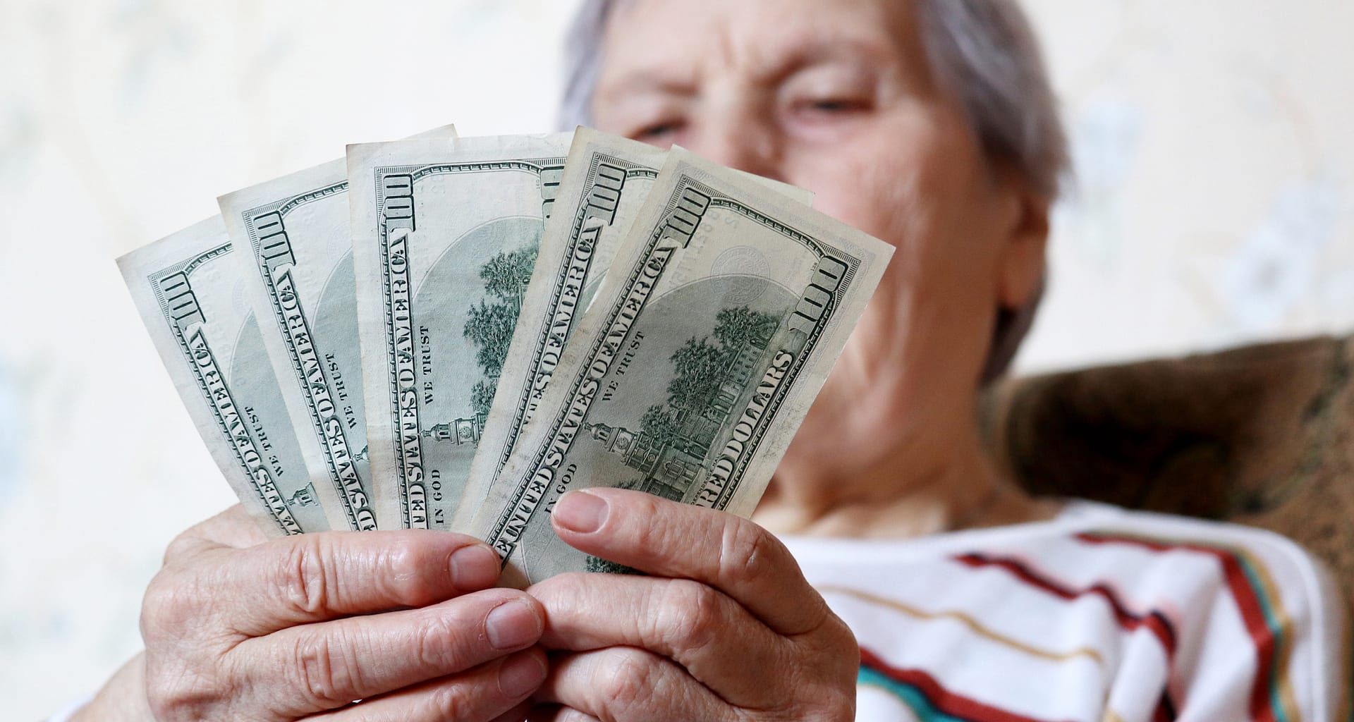 elderly woman retirement social security holding one hundred dollar bills cash getty