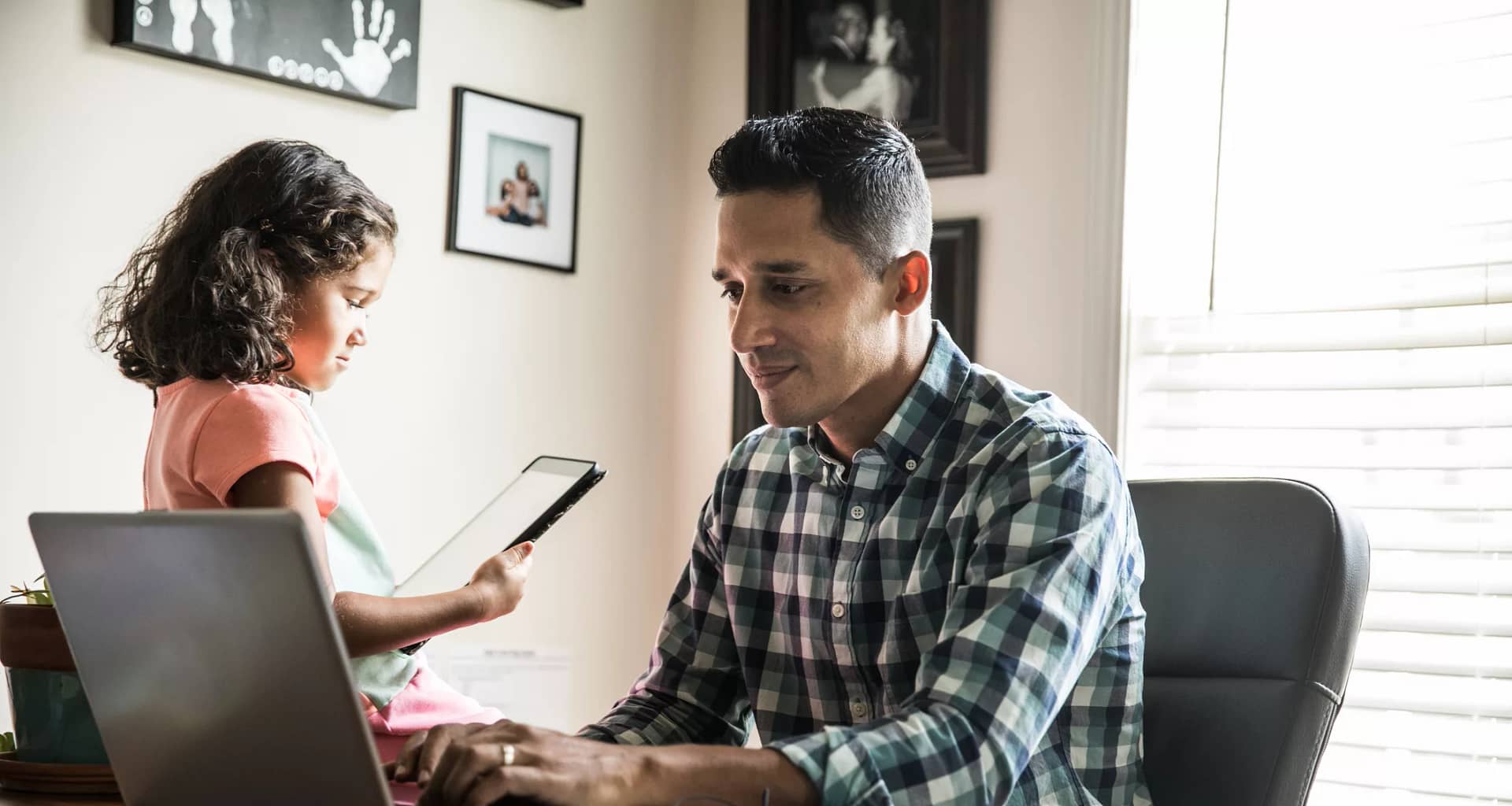 person sitting at a desk looking at a laptop with a child nearby.jpg