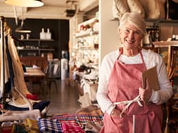 senior woman wearing apron standing next to shelves of apparel in a store small business owner entrepreneur.jpg