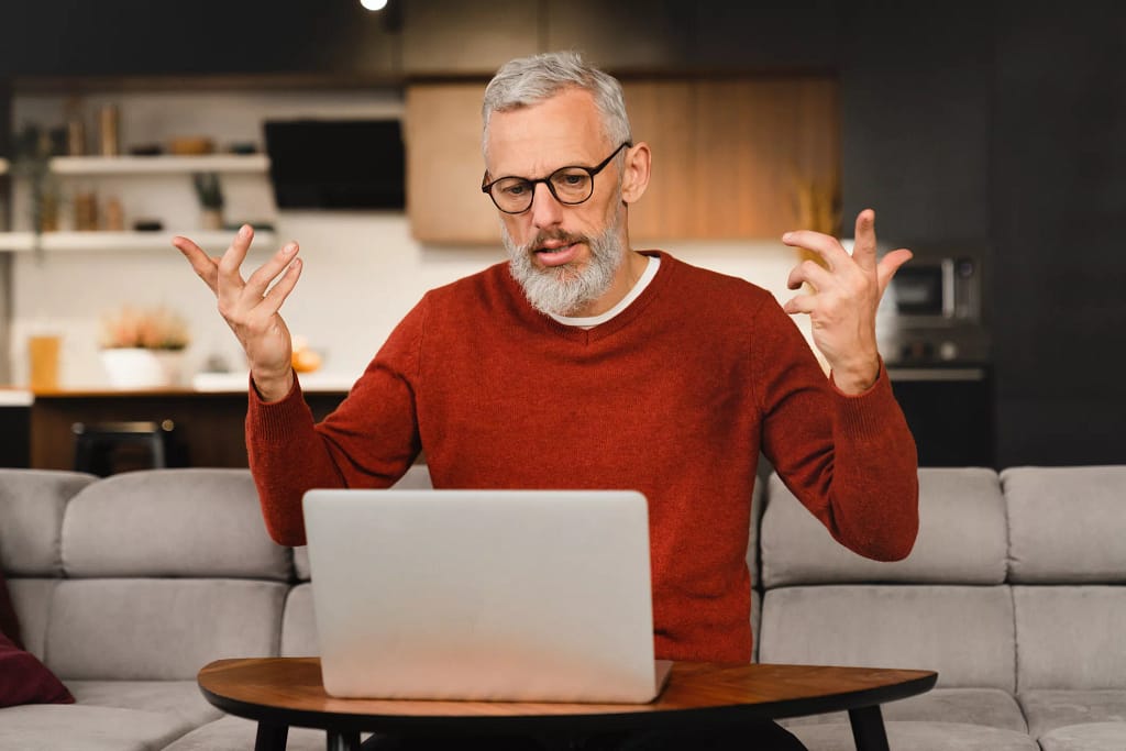 older man at laptop raising his arms as if frustrated.jpg