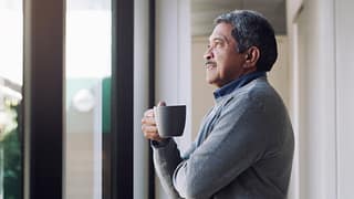 older person holding a mug and looking out a window ifSeK7