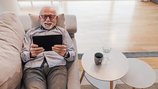 older man lying down on couch holding tablet gettyimages