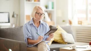 older woman sitting on a couch looking at a calculator
