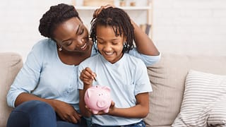 parent and child putting coins into piggy bank at home