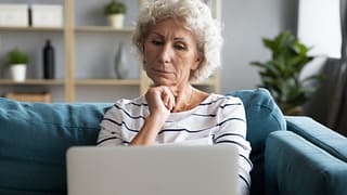 person with hand on chin looking at laptop SFkGg