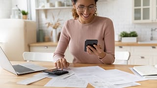 smiling person looking at smartphone and typing on calculator