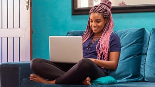 smiling person sitting cross legged on couch using laptop