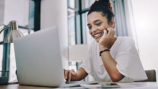 smiling young person with hand on chin looking at laptop GNDUtQ