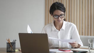 a person sitting at a desk reviewing documents in front of a computer monitor