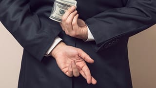 businessman holding cash money bills behind back fingers crossed embezzle getty
