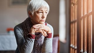 older person sitting at a table looking out a window
