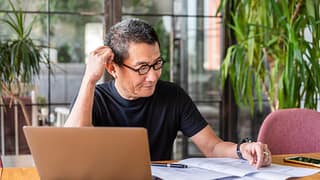 older worker with laptop looking at documents and thinking