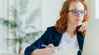 serious person holding pen and looking at laptop