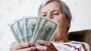 elderly woman retirement social security holding one hundred dollar bills cash getty