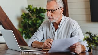 older man laptop holding papers gettyimages