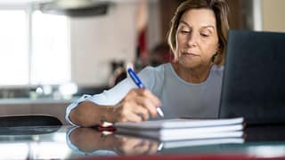older woman taking notes laptop gettyimages