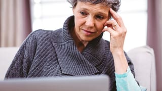 person with a worried expression looking at a laptop