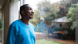 person with serious expression looking out a window