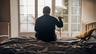 retired man with cane sitting on bed
