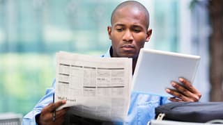 Man reading newspaper and looking at a tablet.width dtWRvy.jpg