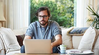 Man sitting on sofa and using laptop at home.width HXjQHwf
