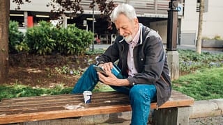 Older gentleman sitting on park bench using h.width Kwa