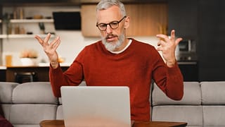 older man at laptop raising his arms as if frustrated gettyimages