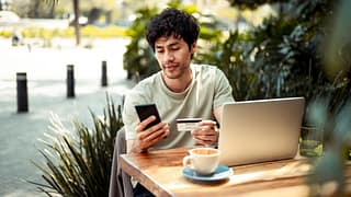 person at outdoor cafe table with laptop phon.width AODczLu.jpg