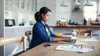 woman at kitchen table with laptop and paperw.width nlFF