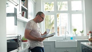 worried man in kitchen with bills fEoJV.width