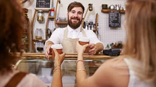 Smiling barista hands coffee to two women PAB.width .jpg