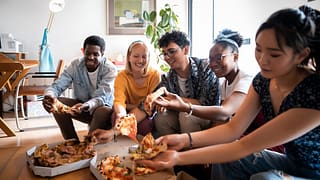 a group of friends eating pizza on an apartme.width DOHqAJ.jpg