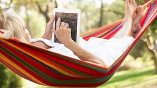 senior woman relaxing in hammock reading ebook.jpg