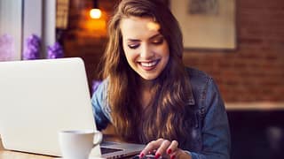 woman smiling with coffee and computer vkYiv.width .jpg