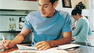young man sitting at kitchen table writing a .width rpvXbE.jpg