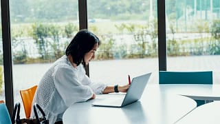 person writing at desk next to laptop DJgfk.width .jpg