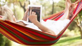 senior woman relaxing in hammock reading ebook.jpg