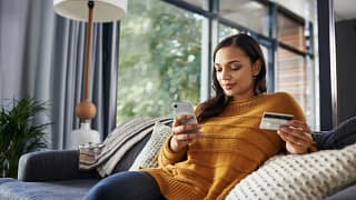 Woman on couch holding phone and credit card .width cWRJtw.jpg