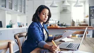 person holding document and writing note with laptop in front of them.jpg