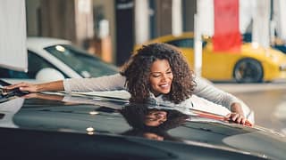 Happy person hugging car at a dealer lot. jhm.width .jpg