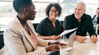 three people sitting at a table smiling and looking at paperwork.jpg
