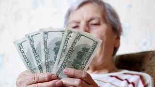 elderly woman retirement social security holding one hundred dollar bills cash getty.jpg