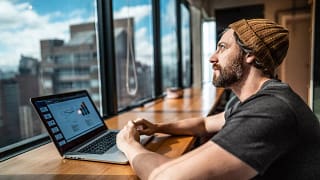 person sitting in front of laptop looking out window of office building.jpg